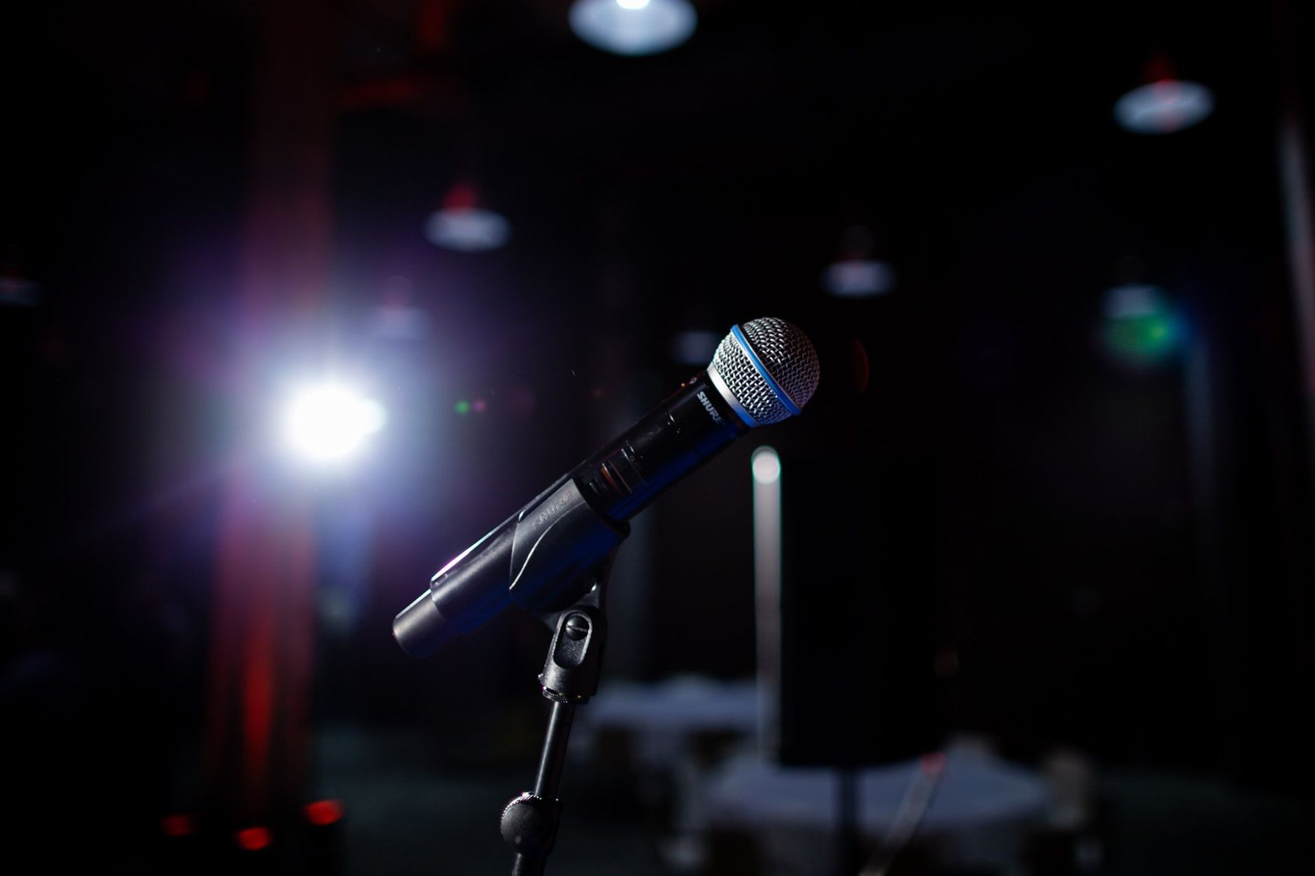 A microphone on a stand under a bright spotlight in a dark club