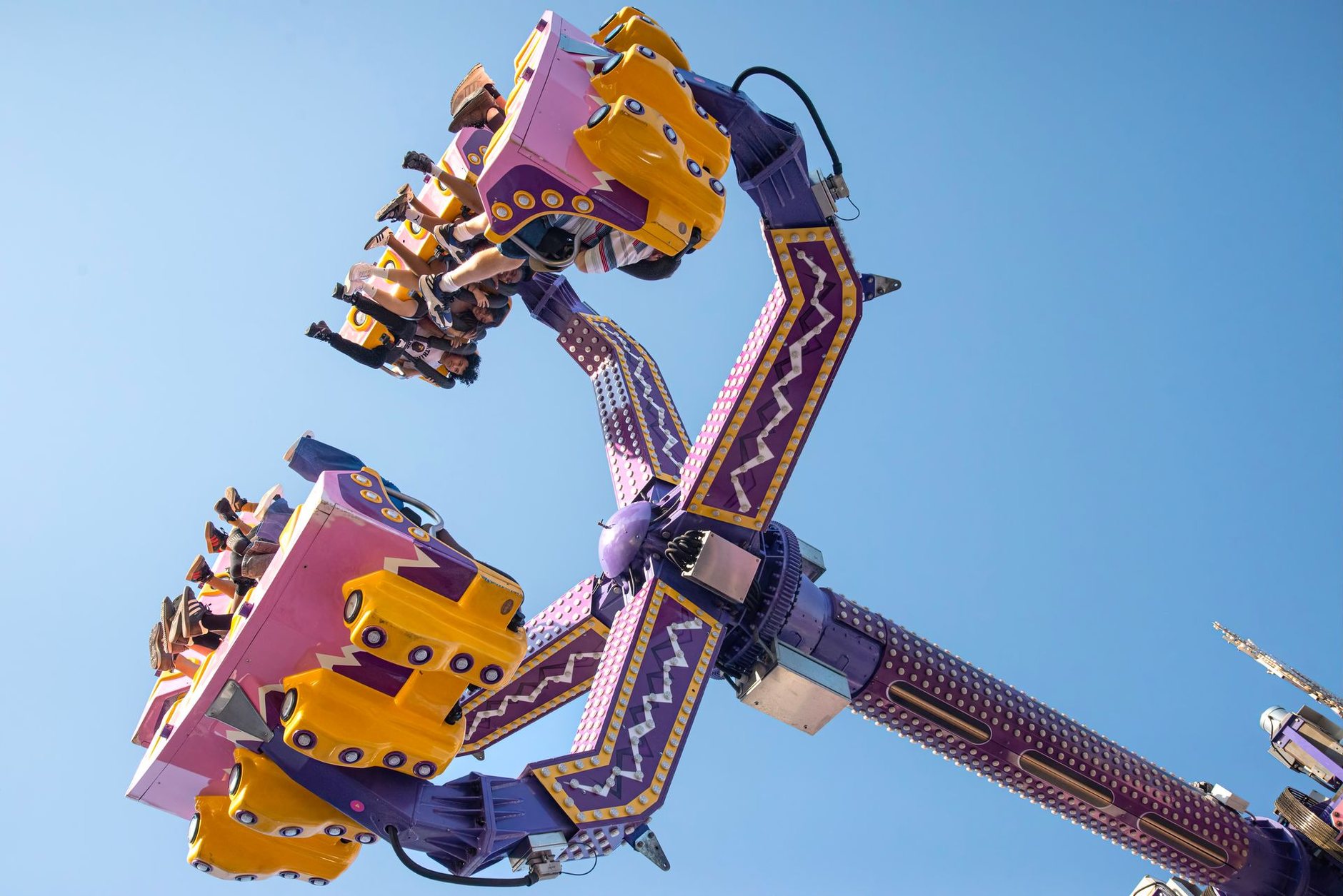 Riders on a spinning thrill ride against a clear blue sky