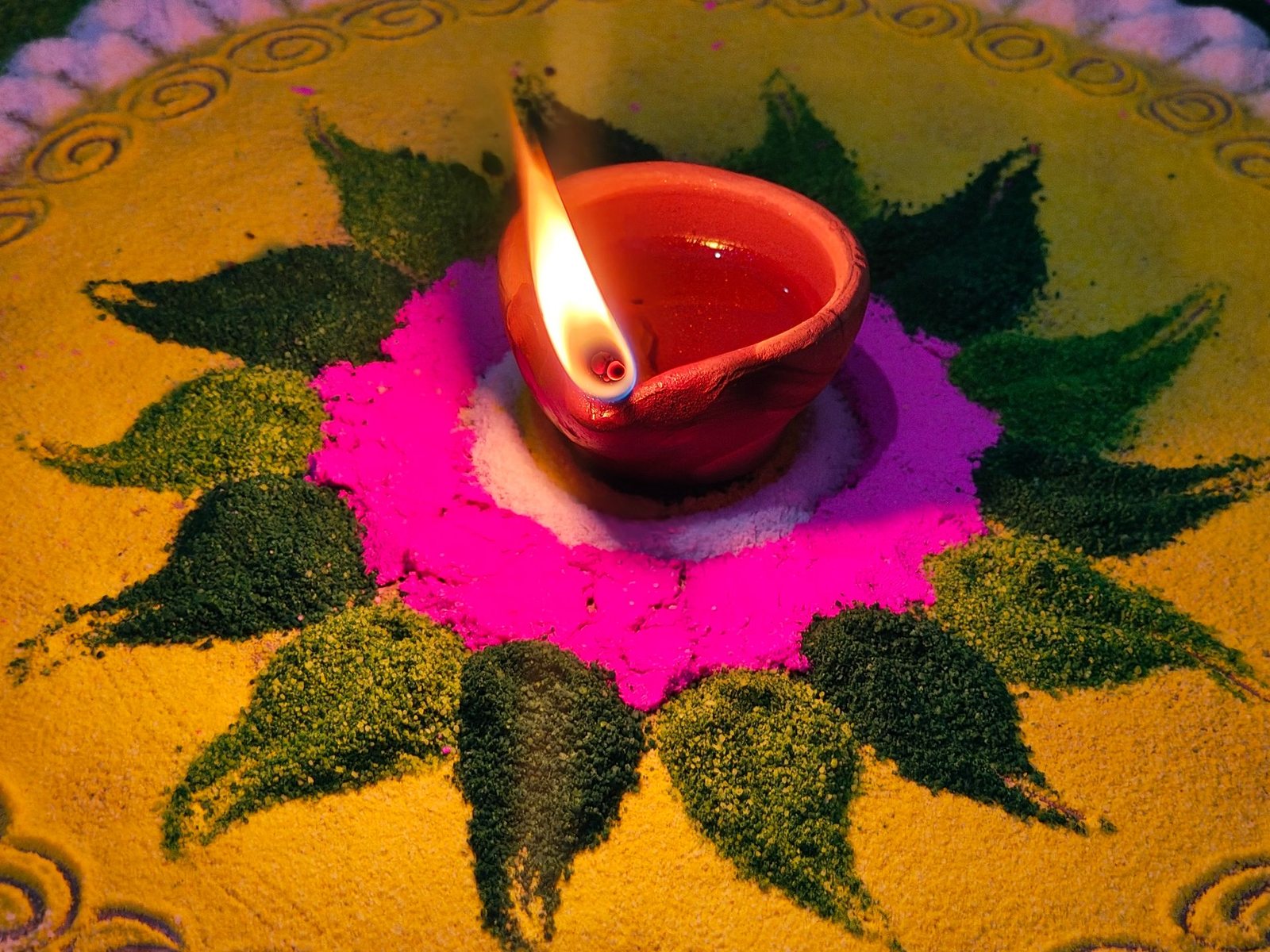 Eine brennende Tonlampe (Diya) in der Mitte eines Rangoli aus gelbem, grünem und rosa Farbpulver