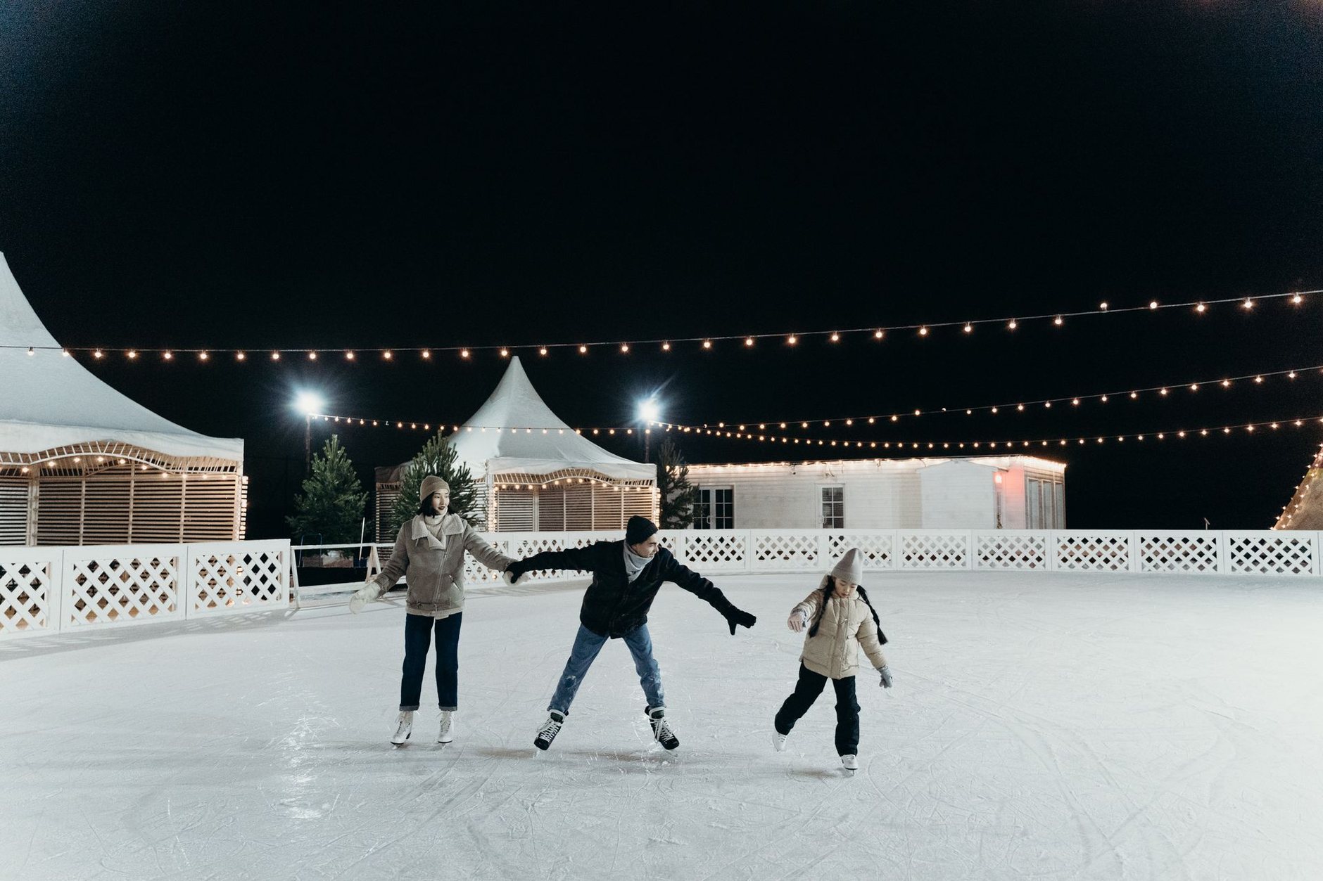Skaters on an outdoor rink at night under strings of lights