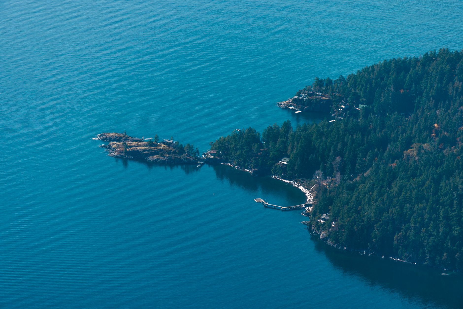 A forested peninsula and small islands in deep blue water, seen from the air