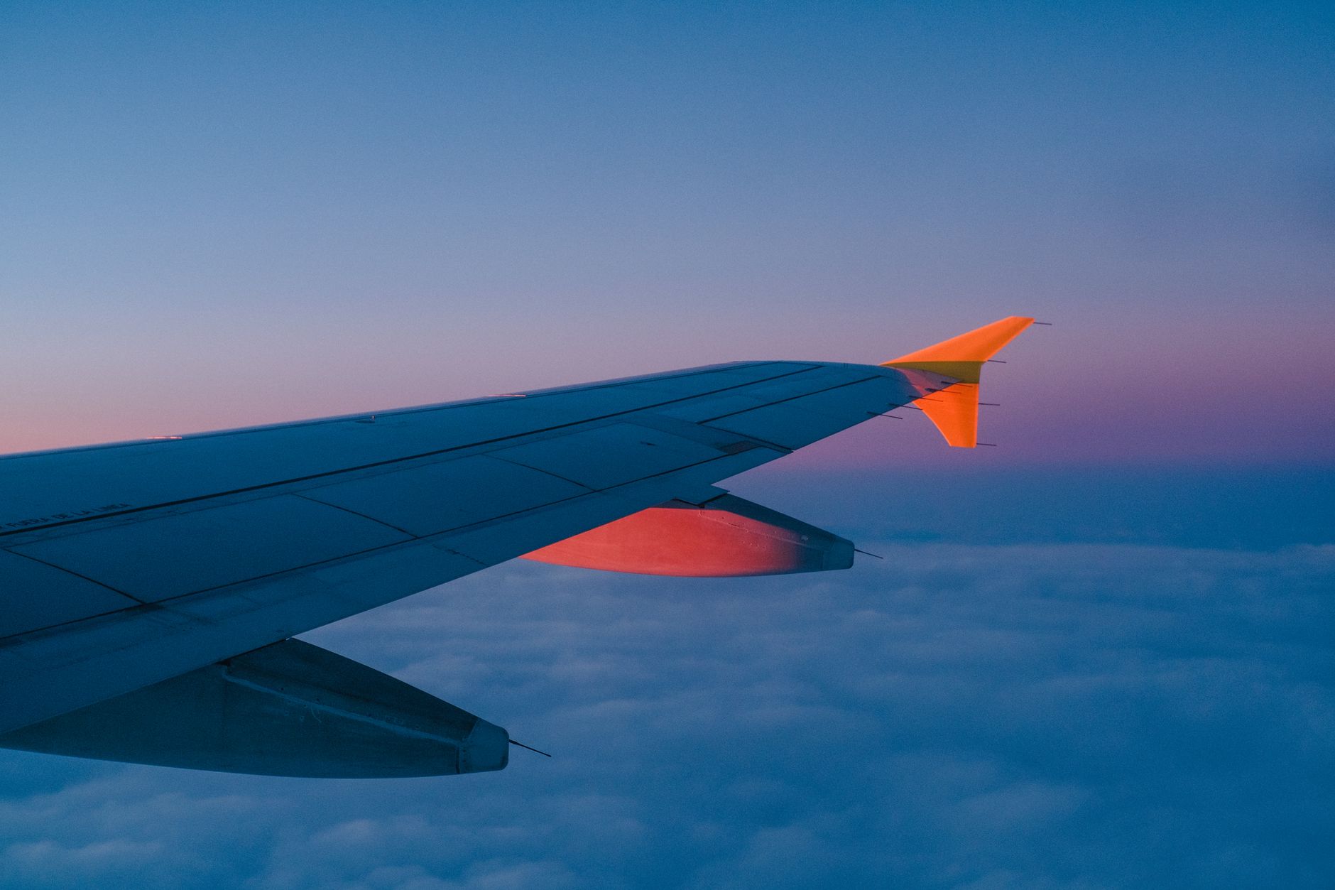 An airliner wing above a layer of cloud at sunset