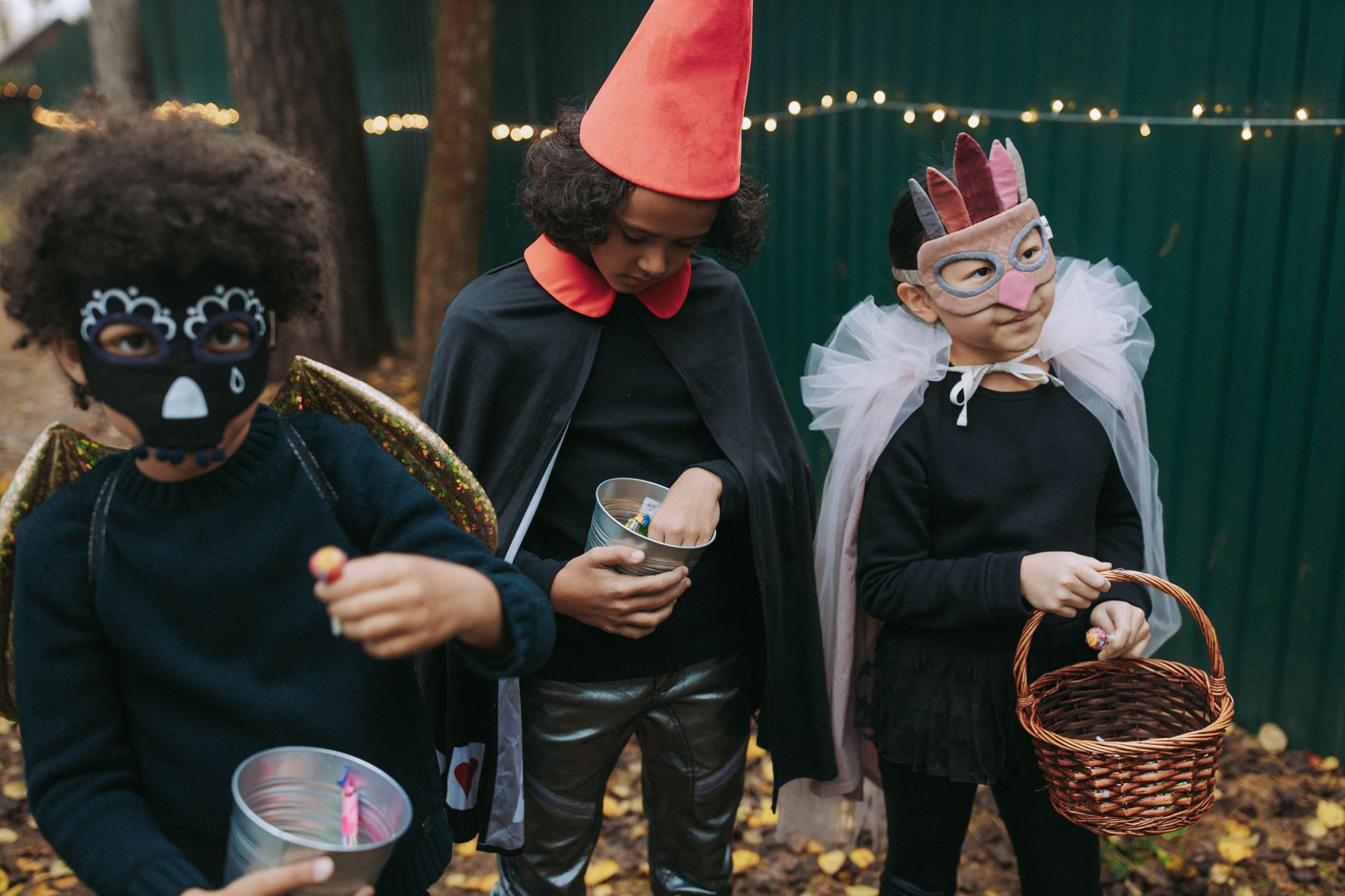 Three children in Halloween costumes collecting candy outdoors on Halloween night