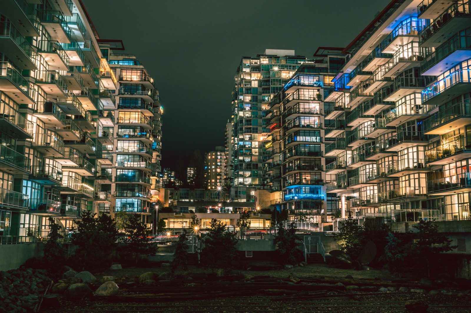 Wohntürme mit beleuchteten Glasbalkonen über einem Uferweg bei Nacht