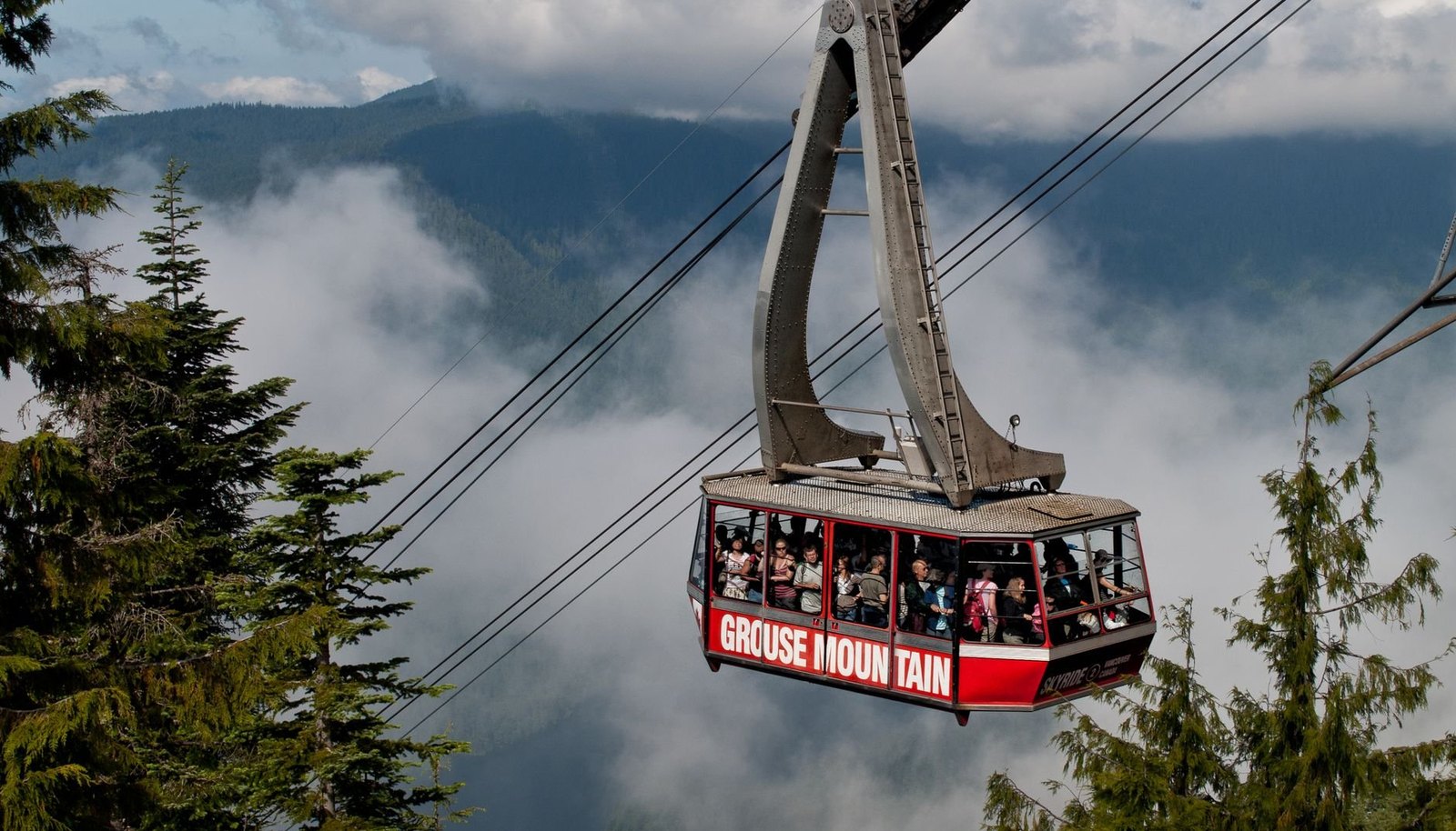 The red Grouse Mountain Skyride gondola full of passengers, rising through cloud above the forest