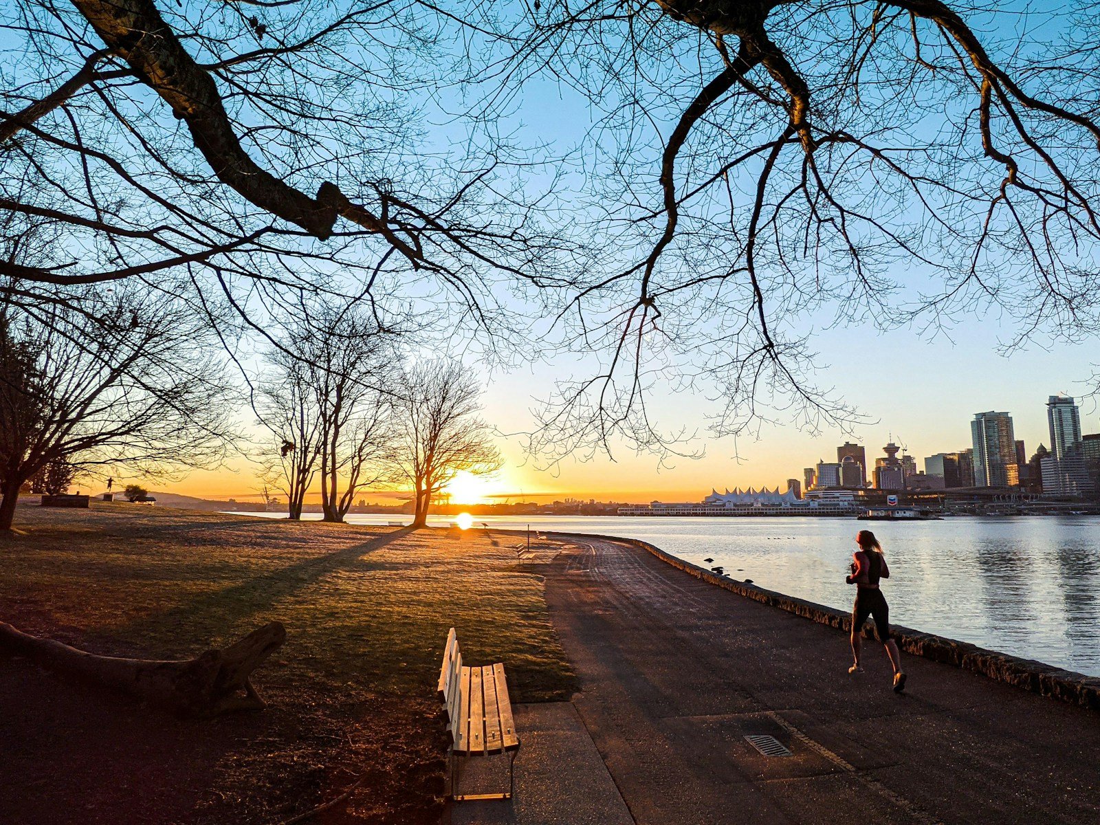 A runner on the Stanley Park Seawall at sunset, with downtown towers across the water