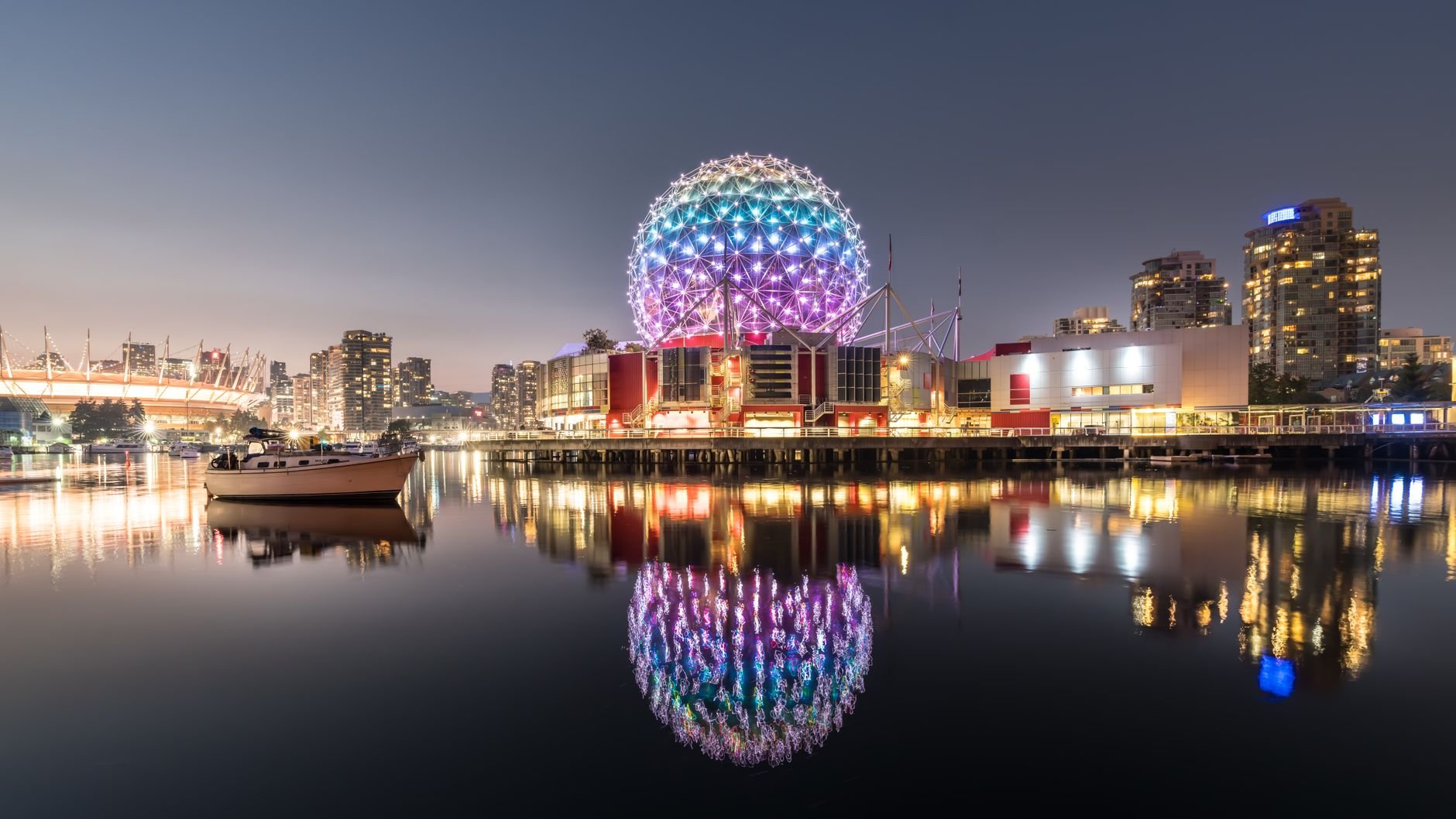 The Science World dome glowing in colour at dusk, reflected in False Creek