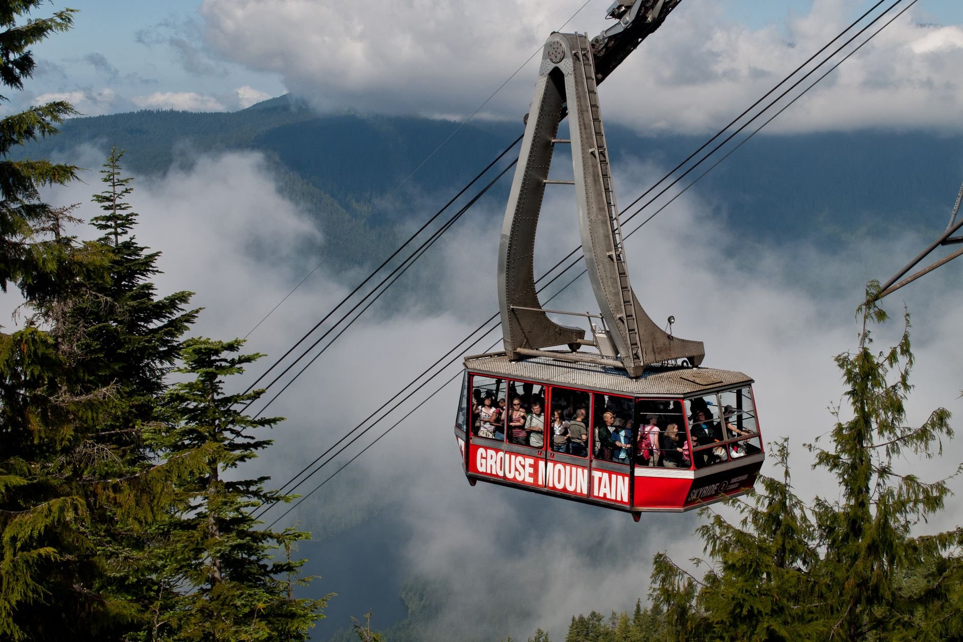 The red Grouse Mountain Skyride cabin rising through cloud above the forest